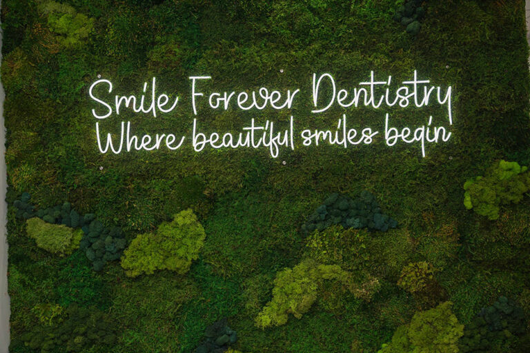 Moss wall with neon sign that says Smile Forever Dentistry - Where beautiful smiles begin
